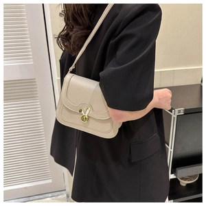 Detail of grey leather crossbody bag featuring a golden bunny ear clasp on a black blazer