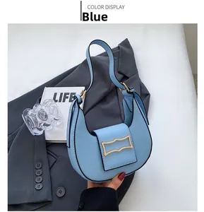 Detail of the blue crescent shoulder bag with golden metallic buckle on a grey blazer