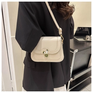 Detail of cream-colored shoulder bag with gold bunny lock worn by a model in office