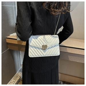 Détail du sac matelassé blanc crème avec fermoir coeur doré sur une robe noire
