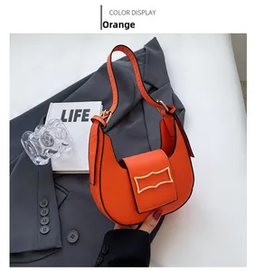 Orange matte leather crescent hobo bag with gold buckle displayed on a grey blazer