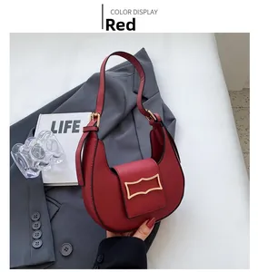 Close-up of red crescent shoulder bag with a gold decorative buckle on a grey blazer