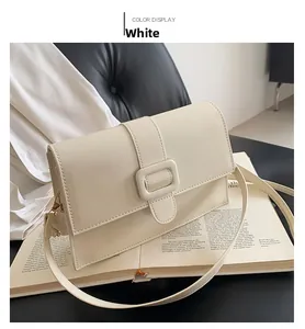 Detail of a creamy white rectangular flap shoulder bag with a square buckle on a book