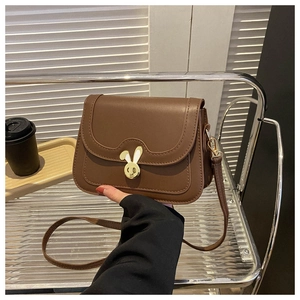 Detail of deep brown crossbody bag featuring a golden rabbit clasp and wavy stitching