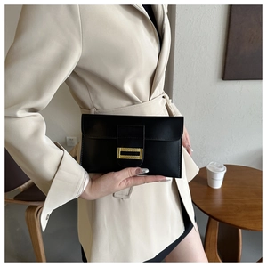 Detail of a chic black leather envelope clutch with a gold buckle held by a model