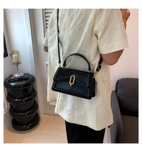 Close-up of minimalist black handbag with elegant gold oval buckle and top handle