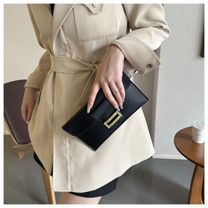 Detail of a black envelope clutch bag featuring a minimalist gold rectangular buckle closure