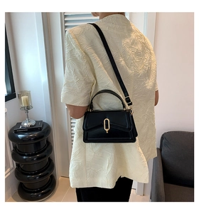 Close-up of stylish black crossbody bag featuring a golden oval twist lock and leather strap