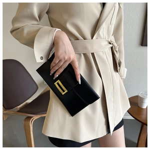 Detail of black leather envelope clutch with a textured gold buckle held by a model