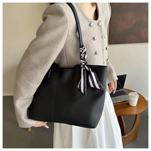 Black tote bag detail featuring textured leather and stylish striped silk scarf handle decor
