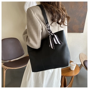Minimalist black leather tote bag with stylish striped silk scarf detail on shoulder strap
