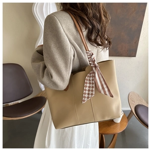 Detail shot of a khaki leather tote bag with a striped silk scarf tied on the handle