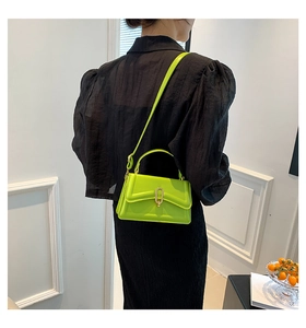 Neon green square crossbody bag with gold U-shaped metal clasp on a black textured top