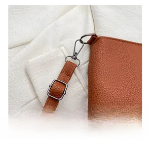 Detail of brown litchi grain leather bag with black metal hooks and adjustable strap