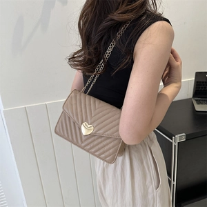 Sac bandoulière matelassé beige avec fermoir cœur et chaîne porté par un mannequin