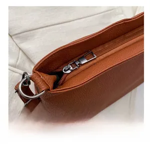 Close-up of smooth metal zipper and D-ring buckle on brown lychee grain leather bag
