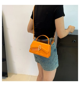 Detail of a bright orange crossbody bag with gold U-shaped lock shown on a model