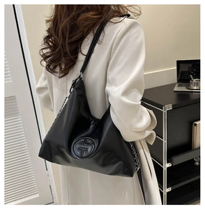 Détail du sac cabas en PU noir avec logo embossé et chaîne argentée porté par un mannequin