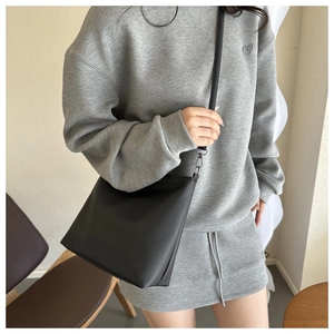 Detailed side view of a black pebble leather bucket bag shown on a model for size comparison
