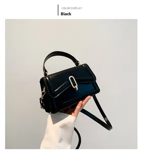 Detail of a black leather crossbody bag with golden U-shaped buckle and hand strap