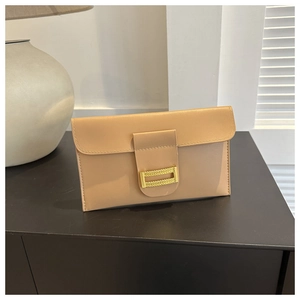 Detail of light beige envelope clutch bag featuring a gold chain link buckle on black wood