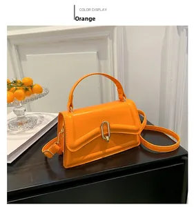 Detail of bright orange PU leather handbag with U-shaped gold buckle and strap