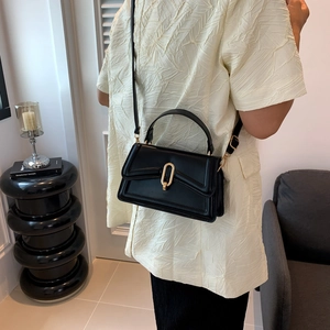 Minimalist black leather crossbody bag with a gold oval lock buckle and handle