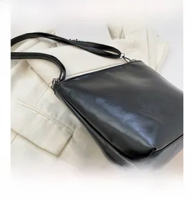 Détail d'un sac seau noir minimaliste avec texture cuir sur un blazer blanc élégant