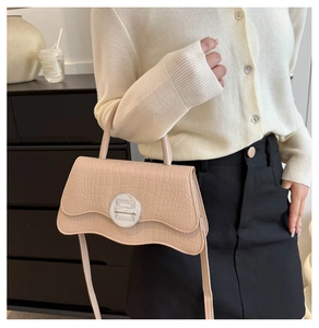Detailed view of beige crocodile pattern handbag with silver clasp on a knit sweater