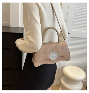 Detail of beige crocodile pattern handbag with wave base and silver clasp worn by model