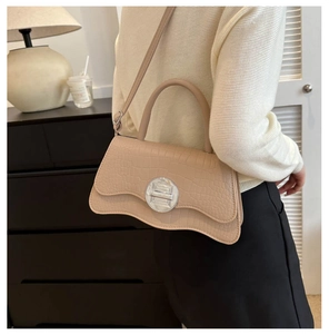 Detail view of beige crocodile embossed handbag with unique asymmetric wavy bottom and metal lock