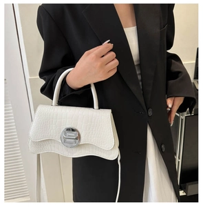 Close-up of a white crocodile embossed handbag with a silver geometric lock and shoulder strap
