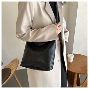 Détail d'un sac seau en cuir noir brillant porté avec un blazer beige chic et moderne
