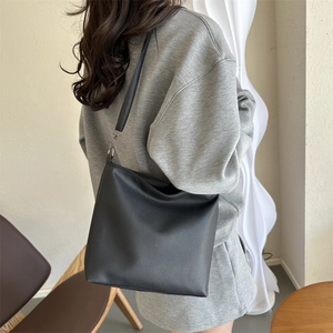 Minimalist black pebbled leather tote bag with slim shoulder strap worn by a model