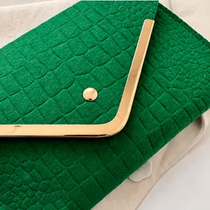 Close-up of emerald green crocodile embossed envelope clutch with gold metal trim