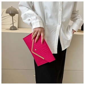 Detail of rose red crocodile embossed envelope clutch bag with gold V-shaped metal trim
