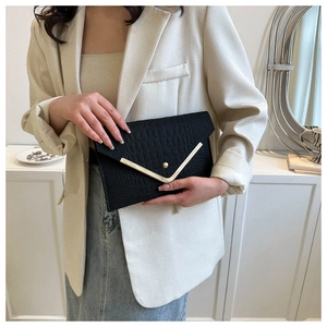 Detail of black faux crocodile leather envelope clutch with V-shaped gold metal trim