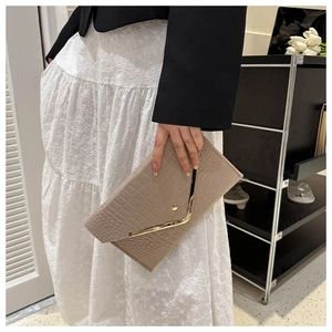 Detail of beige crocodile pattern envelope clutch with gold V-shaped metal trim