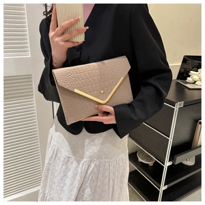 Detail of beige envelope clutch bag with crocodile texture and V-shaped metal trim