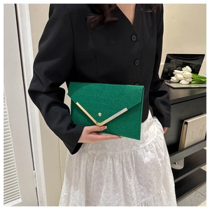 Detail of green crocodile-textured envelope clutch with V-shaped gold metal trim