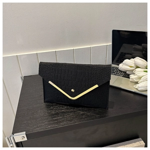 Detailed close-up of a black crocodile-patterned envelope clutch with golden V-trim