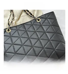 Close-up of black quilted tote bag with triangle stitching and gold chain strap detail