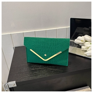 Detail of emerald green faux crocodile envelope clutch with gold V-trim on wood surface