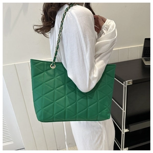 Detail of green quilted tote bag with gold chain strap worn by a model in casual setting