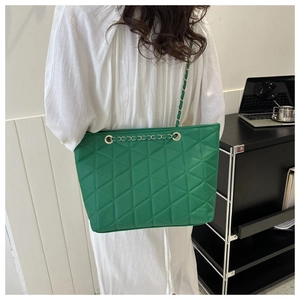 Detail of green triangle quilted shoulder bag with golden chain strap on a model