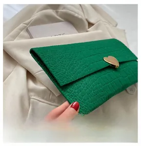 Detail of green crocodile texture envelope clutch bag with gold heart-shaped buckle