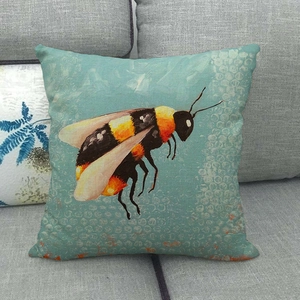 Detail of linen pillow cover featuring a hand-painted bee design on a grey sofa