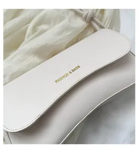 Detailed close-up of cream leather shoulder bag with gold embossed logo on textured fabric