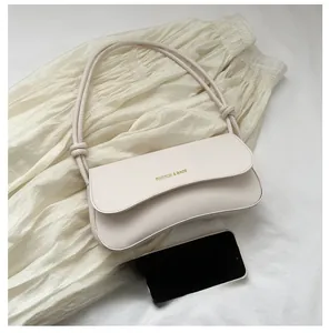 Creamy white leather baguette bag with knotted strap shown next to a smartphone for scale