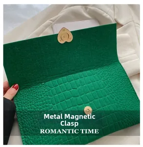 Detail of green faux crocodile envelope bag with gold heart-shaped magnetic buckle